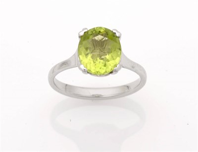 Lot 267 - A Peridot Solitaire Ring, the oval cut peridot in a four claw white setting to a plain polished...