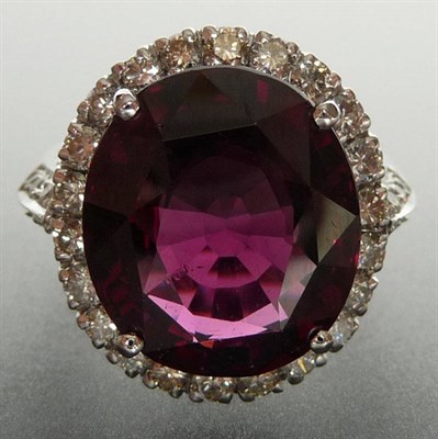 Lot 276 - A Garnet and Diamond Cluster Ring, the oval mixed cut garnet in a white four claw setting sits...