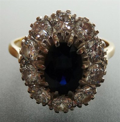 Lot 293 - A Sapphire and Diamond Cluster Ring, the oval mixed cut sapphire in a white claw setting is...