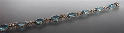 Lot 312 - An Aquamarine and Paste Bracelet, the oval cut aquamarines in claw settings are spaced by cross...