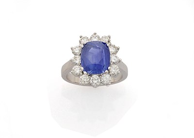 Lot 336 - A Sapphire and Diamond Cluster Ring, the mixed cut sapphire in a white four claw setting is...
