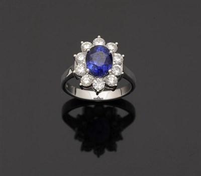 Lot 345 - A Sapphire and Diamond Cluster Ring, the oval mixed cut sapphire in a four claw white setting...