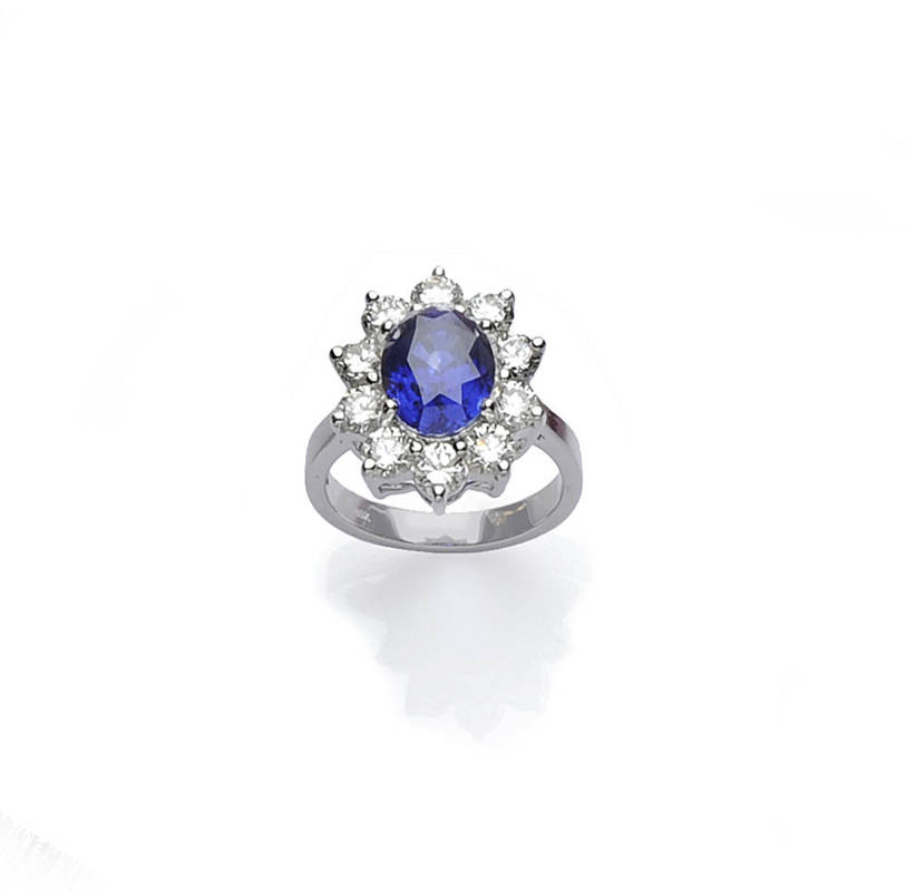 Lot 445 - A Sapphire and Diamond Cluster Ring, an oval mixed cut sapphire within a border of round...