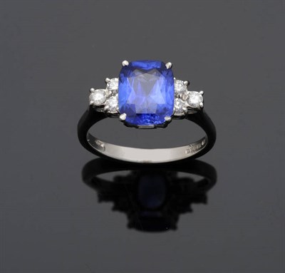 Lot 550 - An 18 Carat White Gold Sapphire and Diamond Ring, the cushion cut sapphire sits between two...