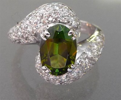 Lot 565 - A Green Tourmaline and Diamond Twist Ring, the oval cut olive green tourmaline in a curved...