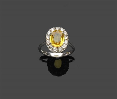 Lot 596 - An 18 Carat White Gold Yellow Sapphire and Diamond Cluster Ring, the oval mixed cut yellow sapphire