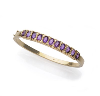 Lot 615 - A 9 Carat Gold Amethyst and Diamond Line Bangle, oval cut amethysts spaced by pairs of tiny...