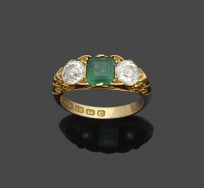 Lot 648 - An Edwardian 18 Carat Gold Emerald and Diamond Three Stone Ring, the step cut emerald flanked by an