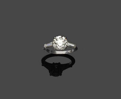 Lot 660 - A Diamond Ring, a round brilliant cut solitaire, with a tapered baguette cut diamond on each...