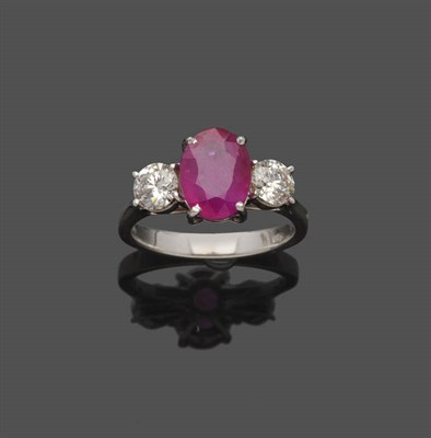 Lot 544 - An 18 Carat White Gold Ruby and Diamond Three Stone Ring, the oval mixed cut ruby is flanked by...