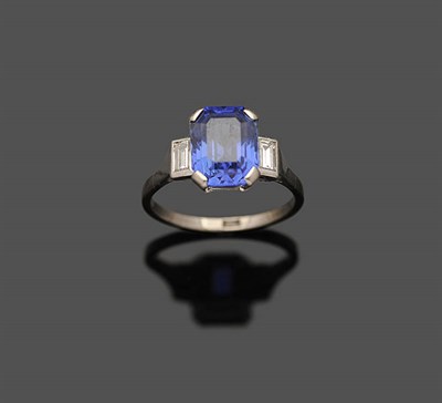 Lot 611 - A Sapphire and Diamond Three Stone Ring, the octagonal step cut sapphire in a white four claw...