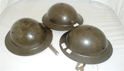 Lot 114 - Three Post Second World War British Army "Brodie" Type Helmets, each with folded rim, rivetted neck