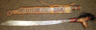 Lot 330 - A Dyak Headhunter's Sword (Mandau), with 50cm hatchet tip steel blade, the wood hilt carved as...