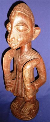 Lot 347 - A Yoruba Carved Wood Figure of Shango, God of Thunder, standing holding a sickle and a club, on...