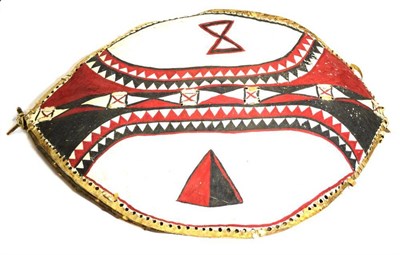 Lot 436 - An African Hide Shield, the white field painted elliptical panels and bands of chevrons in red...