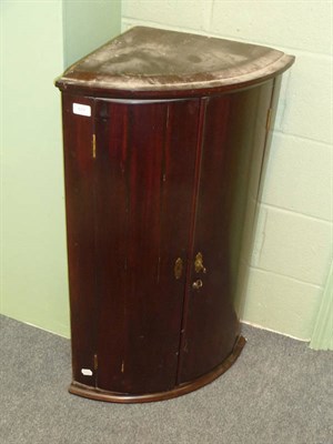 Lot 577 - A Late George III Mahogany Bowfront Hanging Corner Cupboard, the moulded cornice above two cupboard