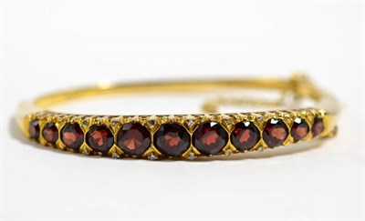 Lot 150 - A 9 carat gold garnet bangle, graduated round cut garnets with single-cut diamond accents, 22.5g