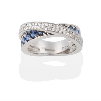 Lot 2021 - An 18 Carat White Gold Sapphire and Diamond Crossover Band Ring, a band of round cut sapphires...