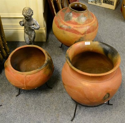 Lot 1177 - Three smoke (pit) fired African earthenware storage pots on cast iron stands