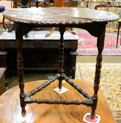 Lot 1302 - A carved oak cricket style table, the circular revolving top with three drop flaps