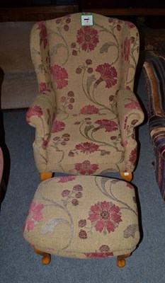 Lot 1493 - ~ A wingback armchair, modern, upholstered in brown floral fabric with rounded arms and squab...