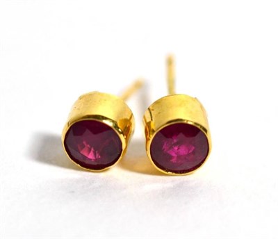 Lot 69 - A pair of 18 carat gold ruby stud earrings, in rubbed over settings, 5.4mm in diameter, with...