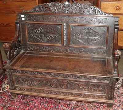 Lot 1309 - A carved oak box settle with dragon carved arms and a leaf and scroll dress rail