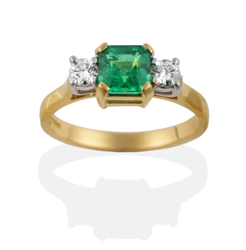 Lot 117 - An 18 Carat Gold Emerald and Diamond Three Stone Ring, the octagonal step cut emerald in four...