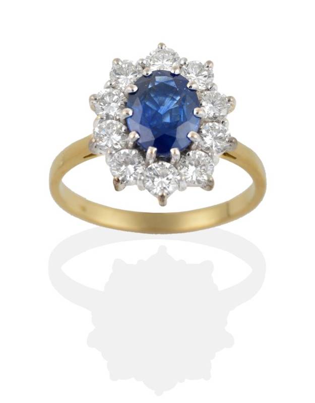 Lot 186 - An 18 Carat Gold Sapphire and Diamond Cluster Ring, the oval mixed cut sapphire within a border...