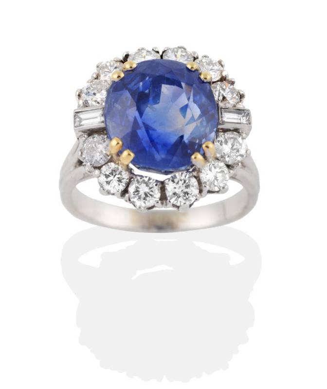 Lot 196 - A Sapphire and Diamond Cluster Ring, an oval mixed cut sapphire of 10.87 carat, in a yellow...