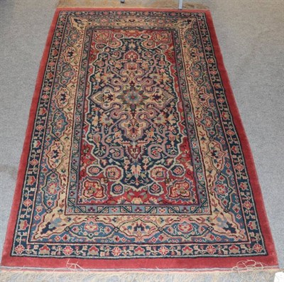 Lot 1254 - Indian rug, the brick red field with an indigo panel and ivory medallion within cartouche...