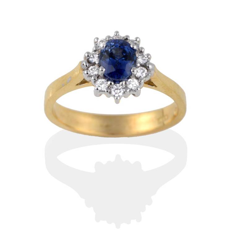 Lot 2005 - An 18 Carat Gold Sapphire and Diamond Cluster Ring, the oval mixed cut sapphire within a border...
