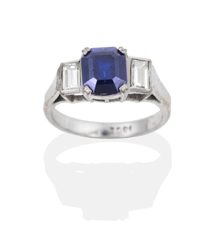 Lot 2041 - A Sapphire and Diamond Ring, an octagonal cut sapphire in a claw setting, to baguette cut...