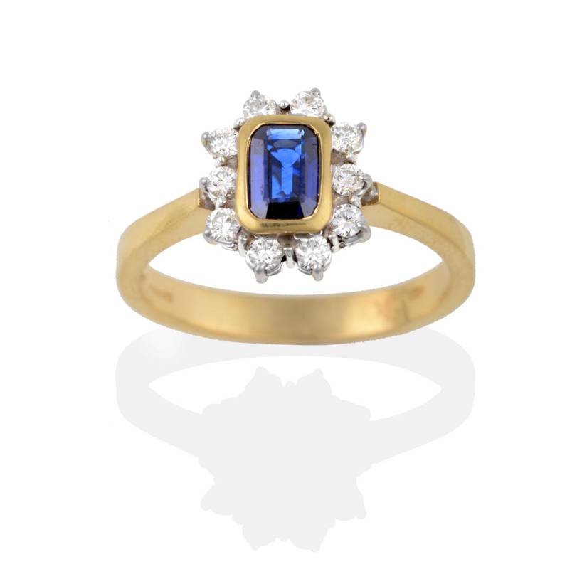 Lot 2152 - An 18 Carat Gold Sapphire and Diamond Cluster Ring, the emerald-cut sapphire in a yellow rubbed...