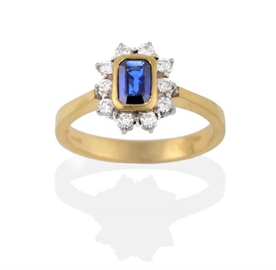 Lot 2152 - An 18 Carat Gold Sapphire and Diamond Cluster Ring, the emerald-cut sapphire in a yellow rubbed...