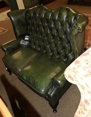 Lot 1344 - A Georgian style buttoned green leather wing back two seater sofa