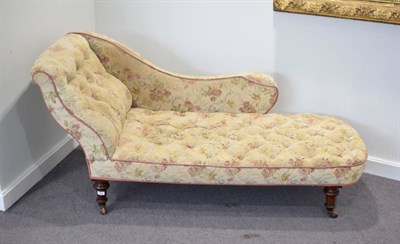 Lot 581 - A Victorian Buttoned Chaise Longue, late 19th century, covered in worn floral fabric, with...