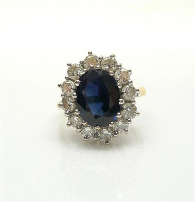 Lot 418 - An 18 Carat Gold Sapphire and Diamond Cluster Ring, the oval mixed cut sapphire within a border...