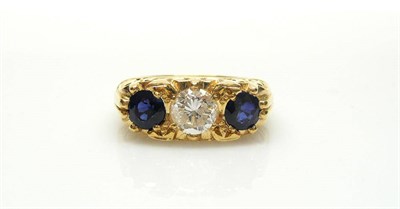 Lot 422 - An 18 Carat Gold Diamond and Sapphire Three Stone Ring, the carved mount holds a round...