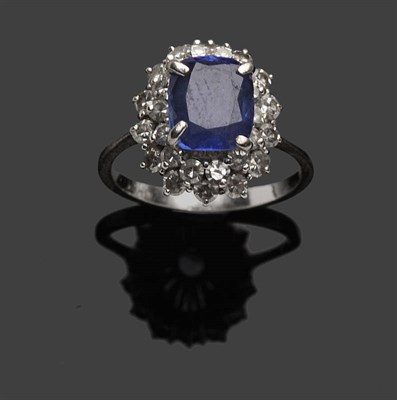 Lot 490 - A Sapphire and Diamond Cluster Ring, the cushion cut sapphire raised above a double row of...