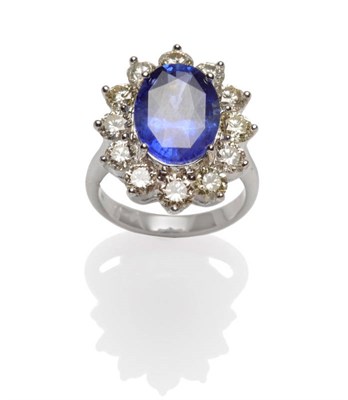 Lot 548 - A Sapphire and Diamond Cluster Ring, the oval mixed cut sapphire within a border of twelve...