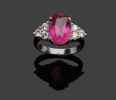 Lot 610 - A Ruby and Diamond Ring, the oval mixed cut ruby flanked by a cluster of three round brilliant...