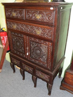 Lot 1402 - A carved oak chest on stand, the upper section with two short above one long drawer with two...