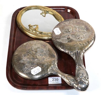 Lot 239 - Two silver cherub decorated dressing table hand mirrors and a small figural oval table mirror...