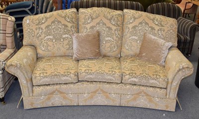 Lot 1242 - A three-seater sofa, modern, of curved form, upholstered in yellow and gold floral fabric, with six