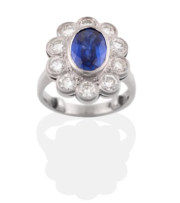 Lot 8 - A Platinum Sapphire and Diamond Cluster Ring, the oval mixed cut sapphire in a rubbed over...