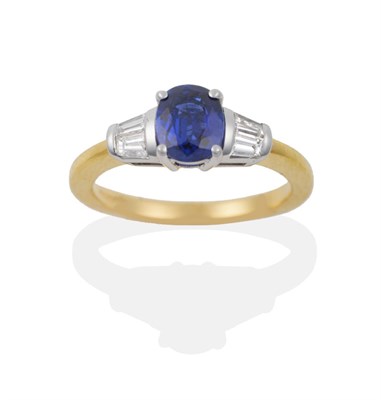Lot 100 - An 18 Carat Gold Sapphire and Diamond Ring, an oval mixed cut sapphire flanked by two tapered...