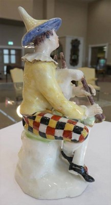 Lot 510 - A Bow Porcelain Commedia dell'Arte Figure of Harlequin, circa 1755, sitting on a rock playing...