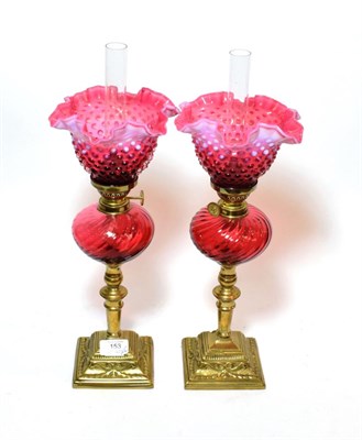 Lot 153 - ^ A pair of cranberry glass oil lamps with brass bases and pink and cranberry glass shades,...