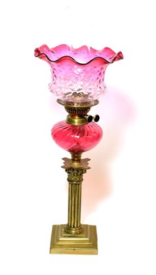 Lot 161 - ^ A Victorian brass oil lamp with cranberry glass reservoir, height excluding chimney 56cm